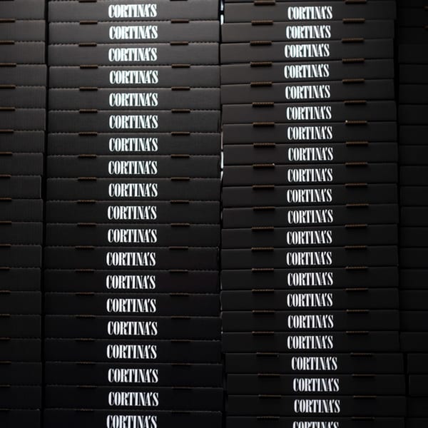 Stacks of black Cortina's pizza boxes with white lettering, ready for delivery.