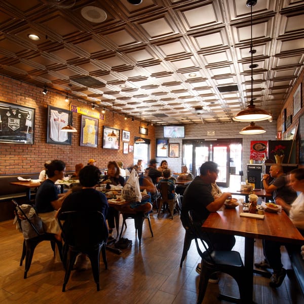 Diners enjoying meals at wooden tables in Cortina's Italian Market & Pizzeria, with brick walls and sports memorabilia.