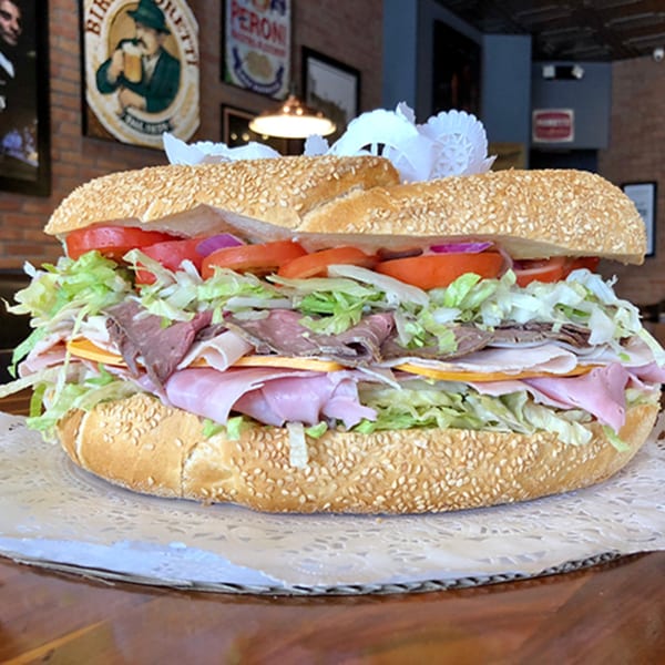 A large, loaded Italian sub sandwich with meats, cheese, lettuce, tomatoes, and onions on a sesame seed roll.