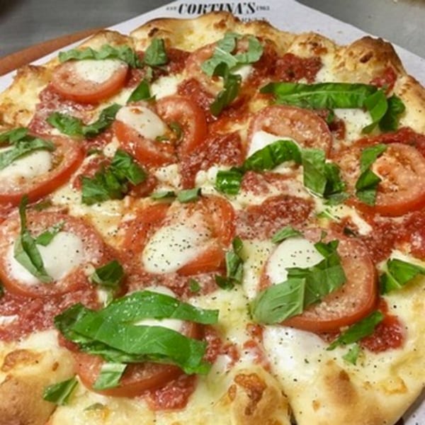 Close-up of a Cortina's Italian Market & Pizzeria Margherita pizza with fresh basil, tomatoes, and mozzarella.