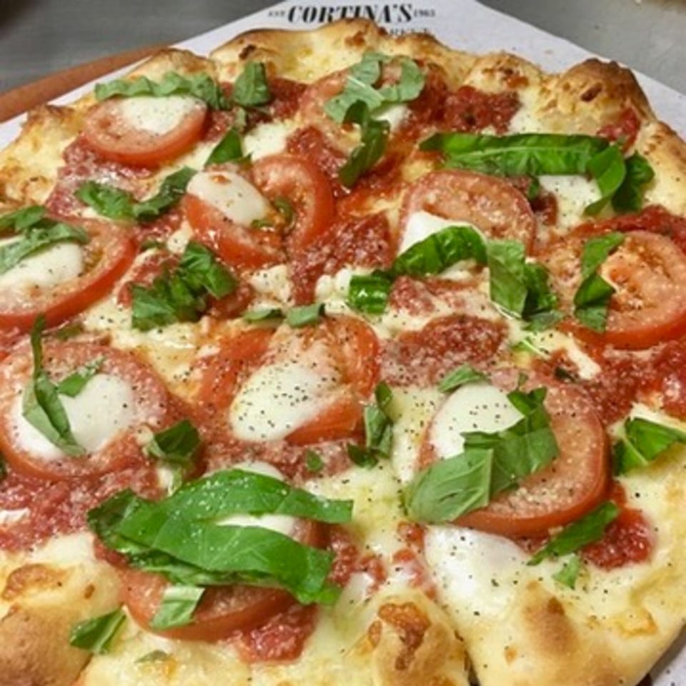 Close-up of a Cortina's Italian Market & Pizzeria Margherita pizza with fresh basil, tomatoes, and mozzarella.