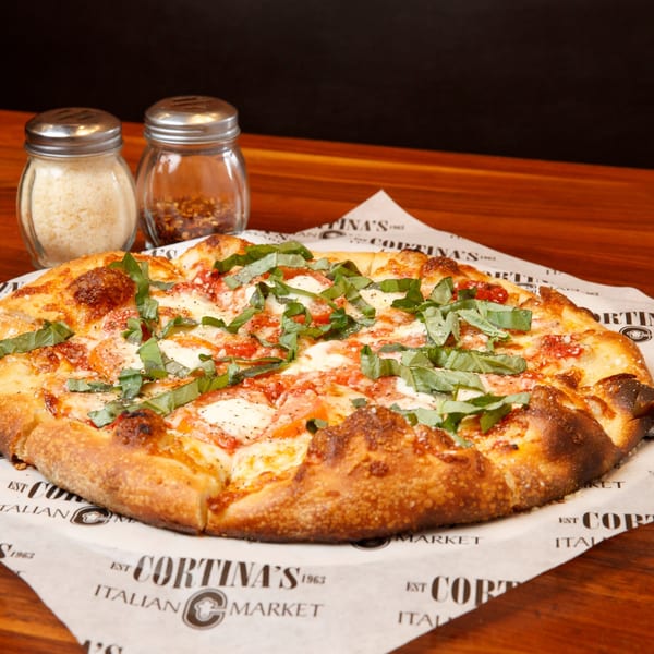 A Cortina's Italian Market & Pizzeria Margherita pizza with basil, cheese, and tomato on branded paper.
