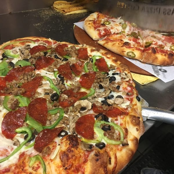 Two pizzas, one with pepperoni, sausage, peppers, mushrooms, and olives, the other with pepperoni and jalapeños.