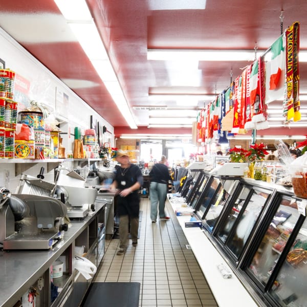 Cortina's Italian Market deli counter with meat slicers, canned goods, and Italian flags hanging overhead.