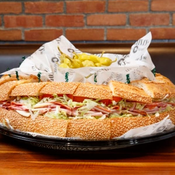 A large Italian sub sandwich with lettuce, tomato, and deli meats, served with pickled peppers.