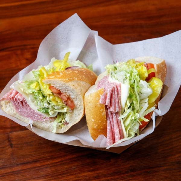 Two halves of a Cortina's Italian Market & Pizzeria sub sandwich, filled with meats, cheese, lettuce, and peppers.