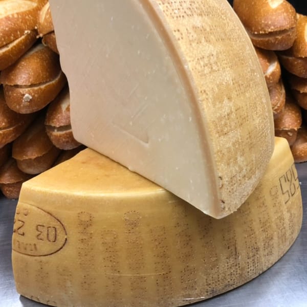 Two large wedges of Italian cheese, one on top of the other, with bread rolls in the background.