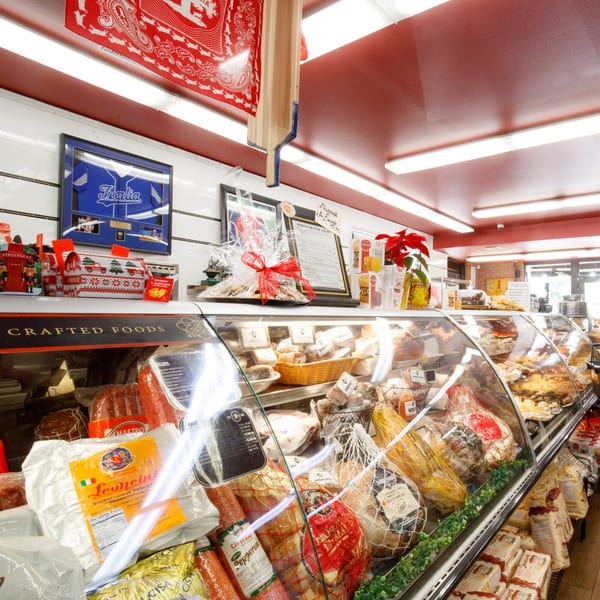 A deli case at Cortina's Italian Market filled with various Italian meats, cheeses, and packaged goods.