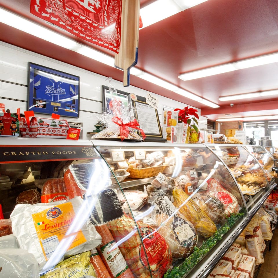 A deli case at Cortina's Italian Market filled with various Italian meats, cheeses, and packaged goods.