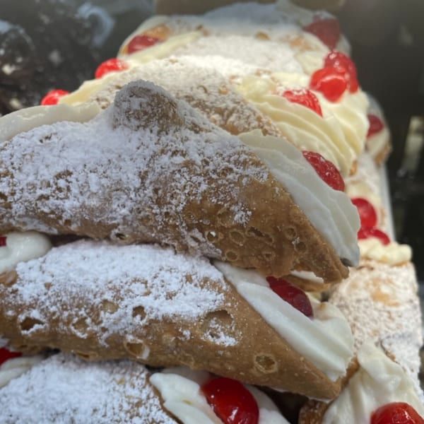 Close-up of several cannoli from Cortina's Italian Market, filled with cream, topped with cherries and powdered sugar.