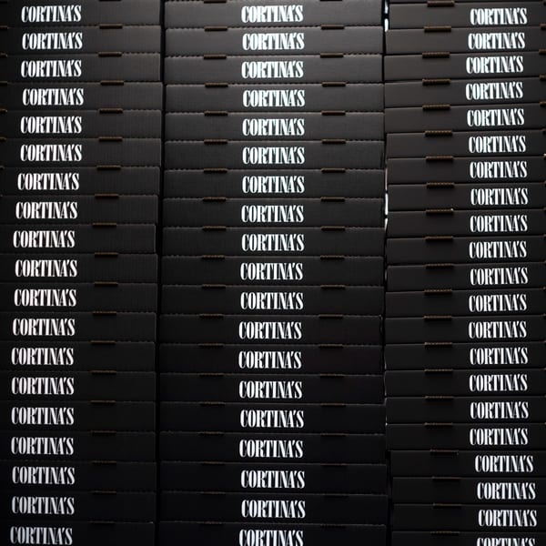Stacks of black pizza boxes with "CORTINA'S" printed in white on each, ready for delivery.