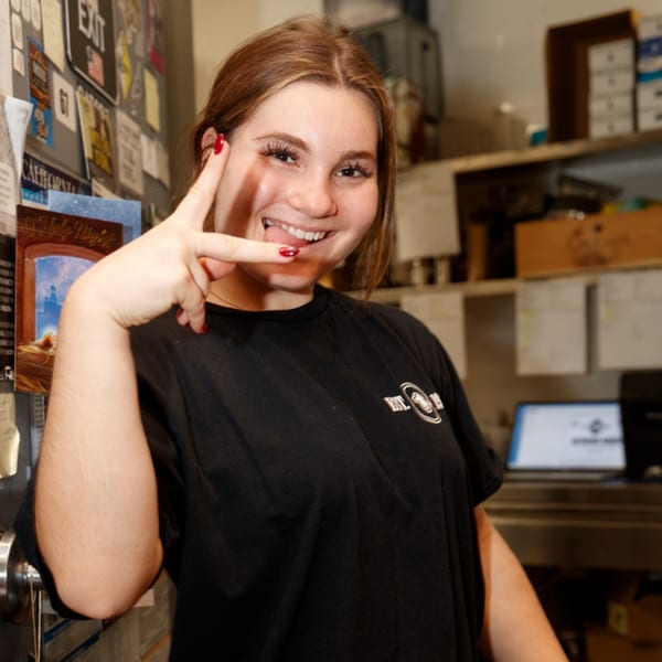 Smiling Cortina's Italian Market & Pizzeria employee making a peace sign in the kitchen.