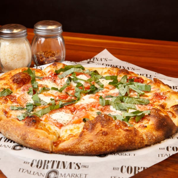 A Cortina's Italian Market & Pizzeria Margherita pizza with basil, cheese, and tomato, with shakers.