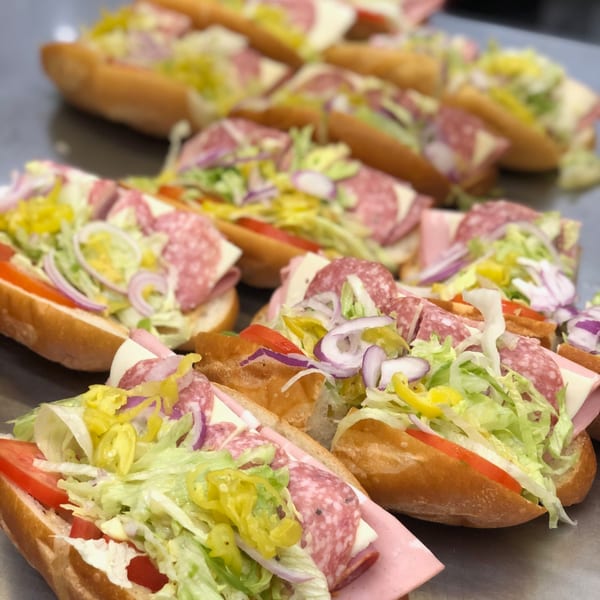 Multiple Italian subs with salami, ham, cheese, lettuce, tomatoes, onions, and peppers.