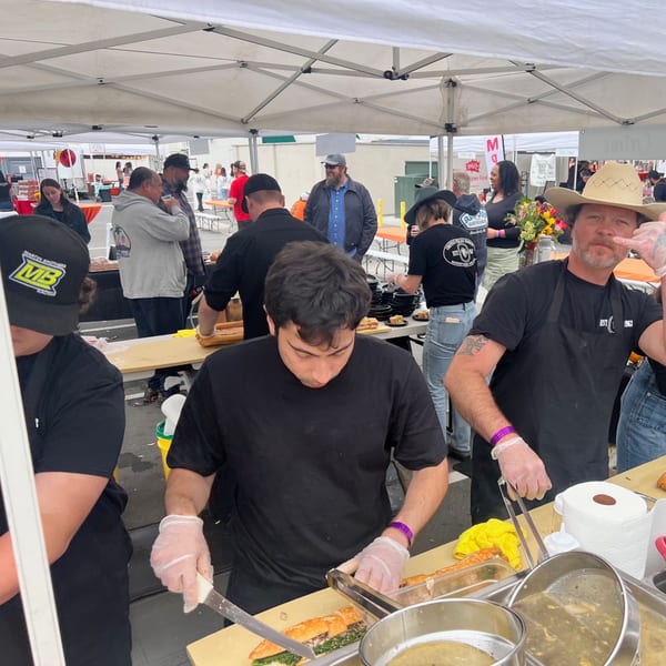 Cortina's staff preparing Italian sandwiches and food at an outdoor market stall under a white tent.
