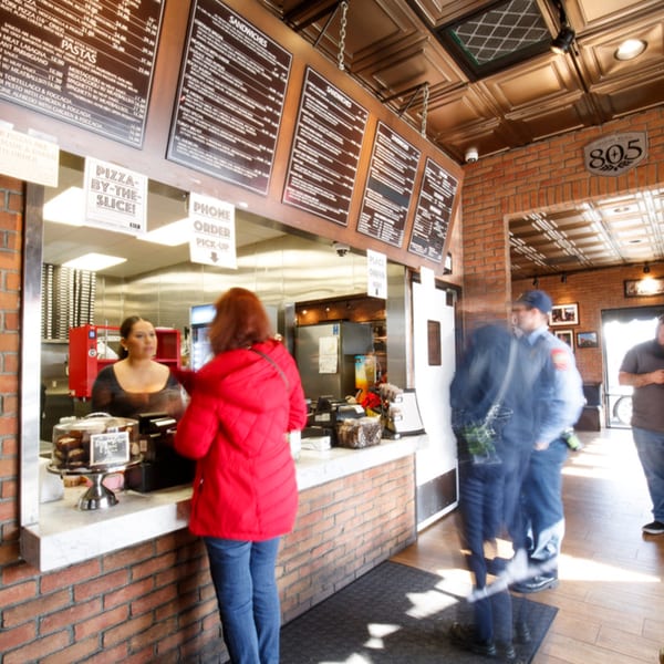 A customer in a red jacket orders at the counter of Cortina's Italian Market & Pizzeria.