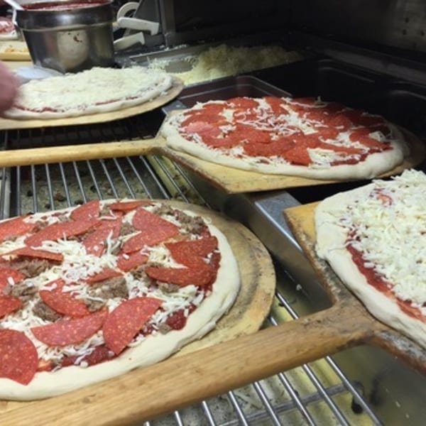 Multiple uncooked pizzas with various toppings, including pepperoni and sausage, on wooden peels.