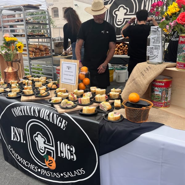 Cortina's Italian Market & Pizzeria outdoor booth with sandwiches, bread, and staff.