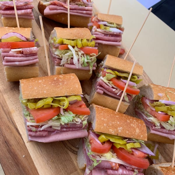 Several Italian deli sandwiches, cut in half, with various meats, cheese, lettuce, tomatoes, and peppers.