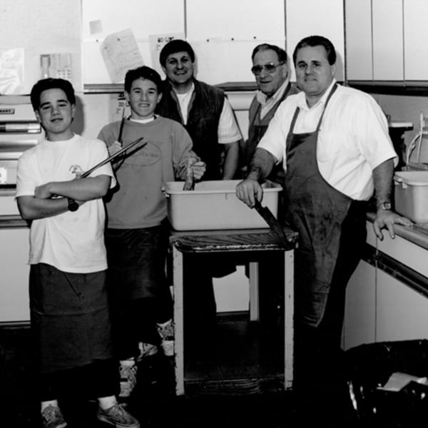 Five men, likely family, in aprons and casual clothes, preparing food in a kitchen.