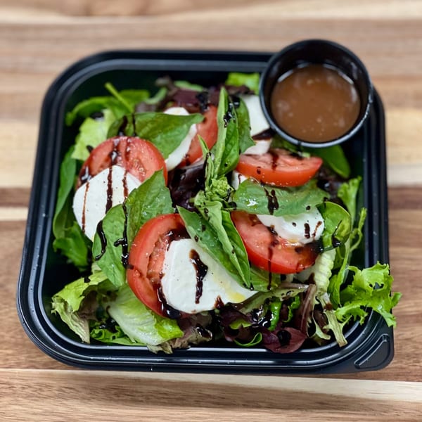 A fresh Caprese salad with tomatoes, mozzarella, basil, and balsamic glaze in a black container.