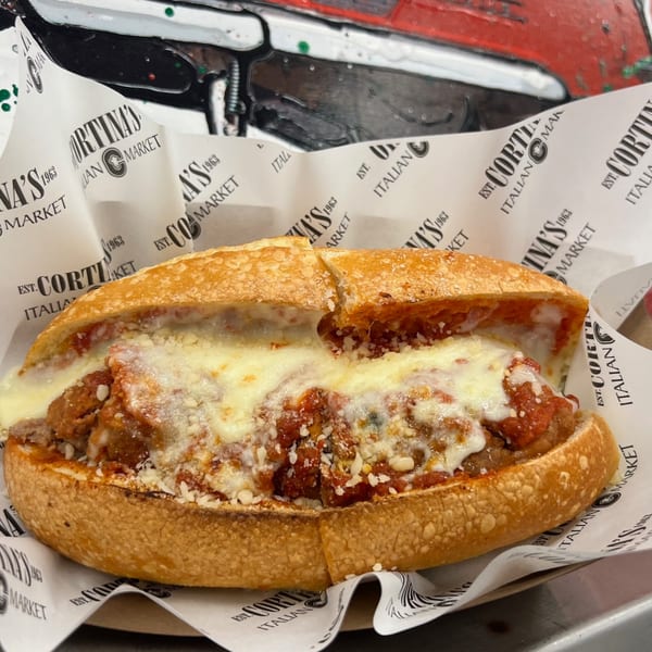 A Cortina's meatball sub, overflowing with marinara sauce and melted cheese, on branded paper.