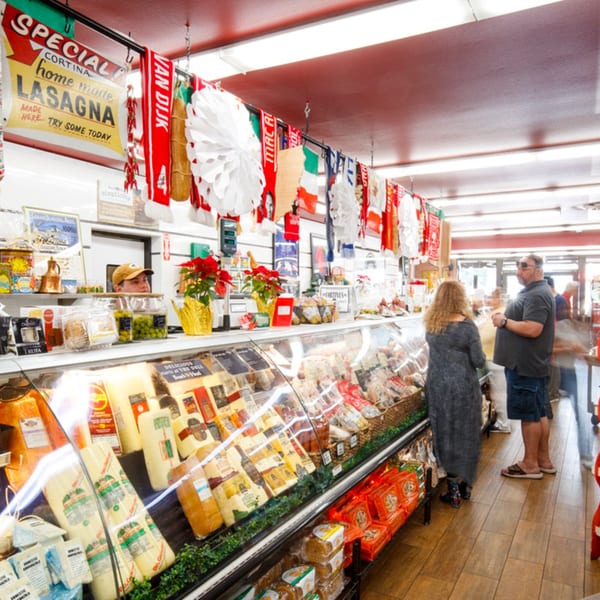 Customers browse a deli counter filled with cheeses and Italian goods at Cortina's Italian Market.
