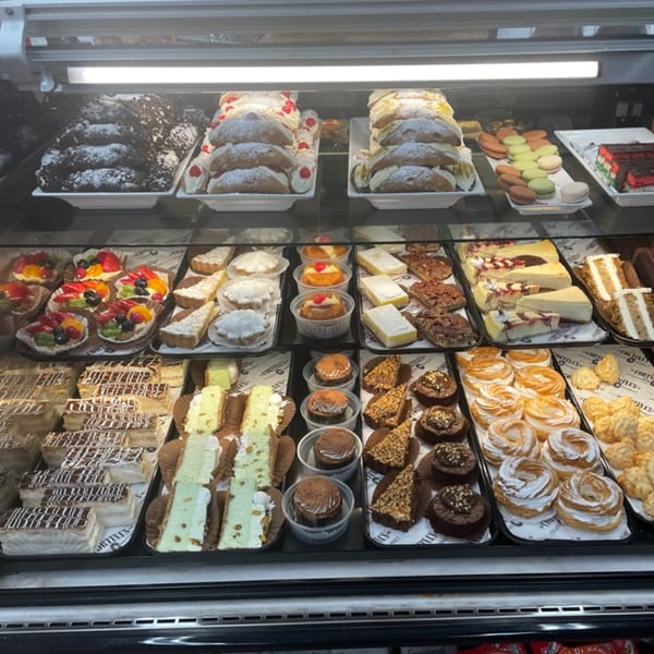 A brightly lit display case filled with various Italian pastries, cakes, and desserts at Cortina's.