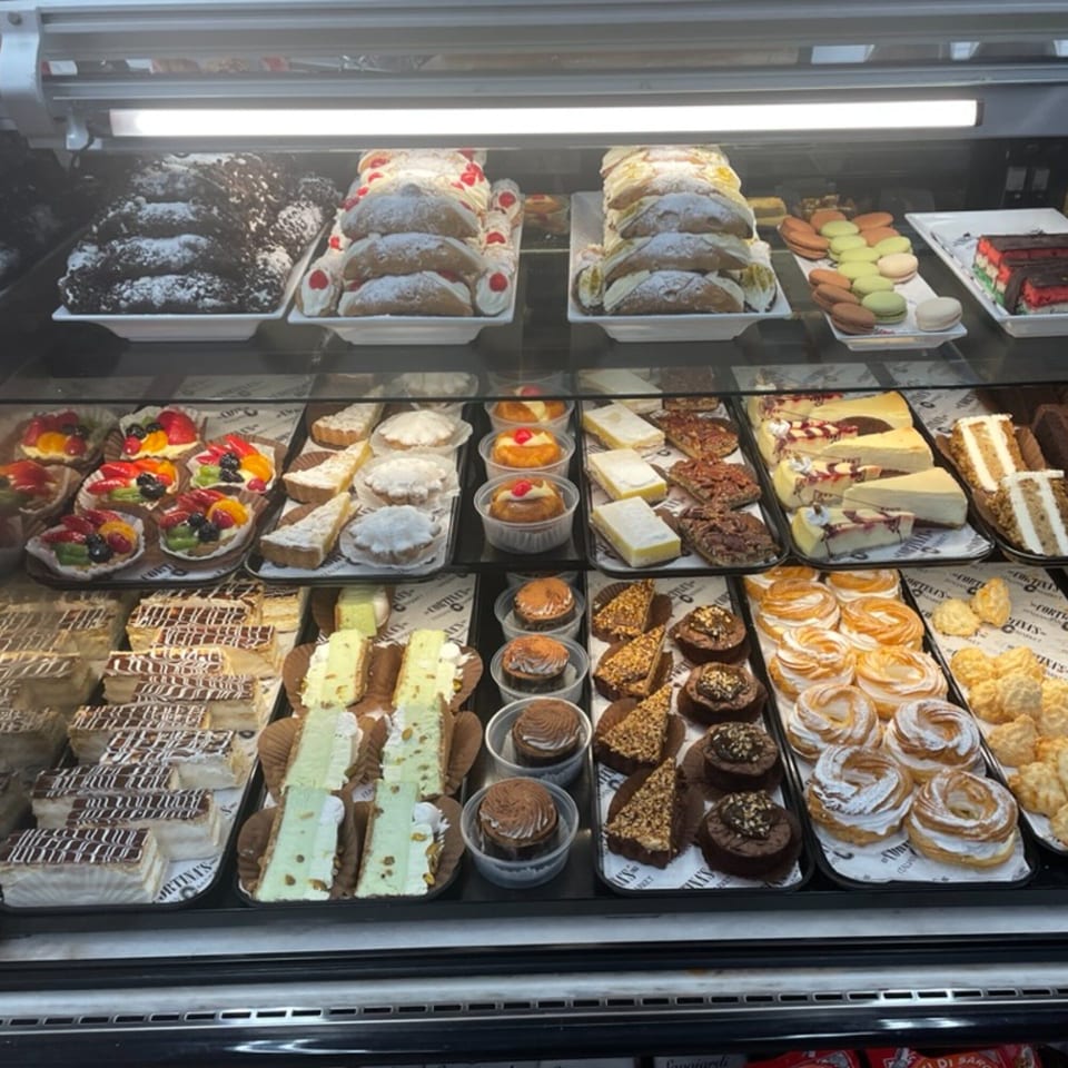 A brightly lit display case filled with various Italian pastries, cakes, and desserts at Cortina's.