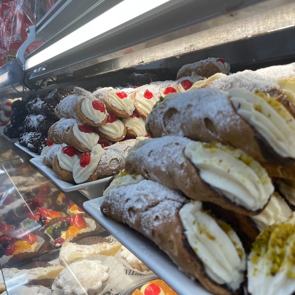 A display case filled with various Italian pastries, including cannolis topped with cherries and pistachios.