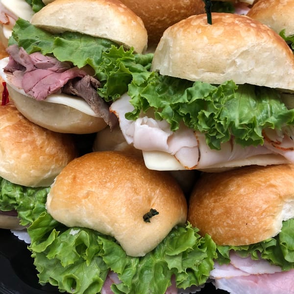 Close-up of various deli meat and cheese sliders with lettuce on small buns.