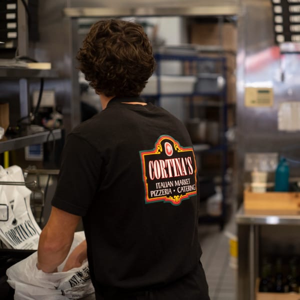 A Cortina's Italian Market & Pizzeria employee in a black shirt working in the kitchen.