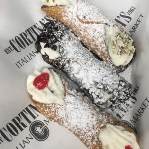 Three cannolis, one with pistachios, one with chocolate chips, and one with a cherry, on branded paper.