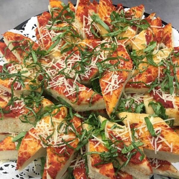 Triangular slices of focaccia bread with tomato sauce, shredded cheese, and fresh basil on a platter.