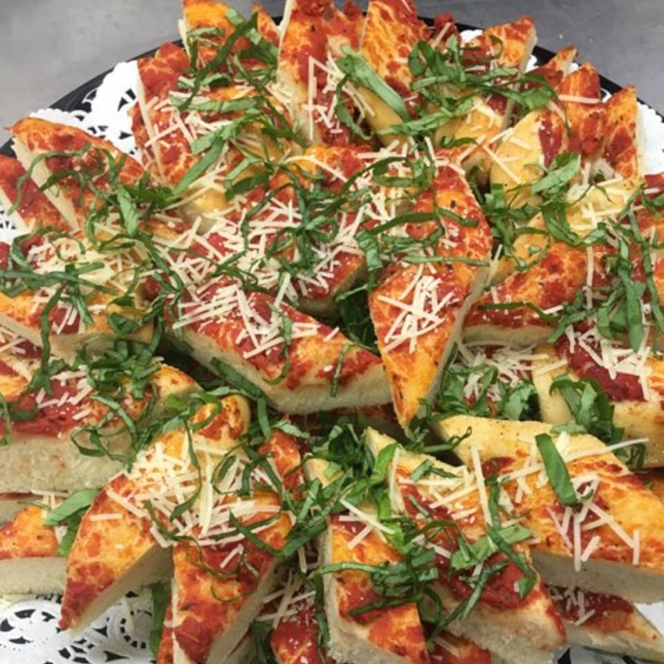 Triangular slices of focaccia bread with tomato sauce, shredded cheese, and fresh basil on a platter.