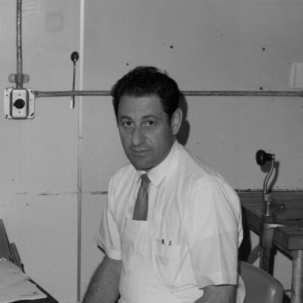 Black and white portrait of a man in a short-sleeved shirt and tie, looking at the camera.