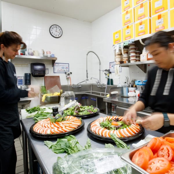 Two chefs prepare multiple Caprese salads and mixed green salads in a busy Italian kitchen.