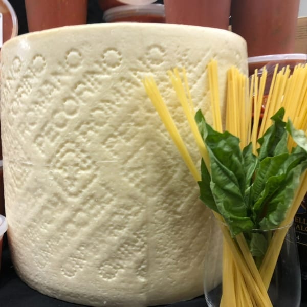 A large wheel of Pecorino cheese next to a glass of spaghetti and fresh basil.