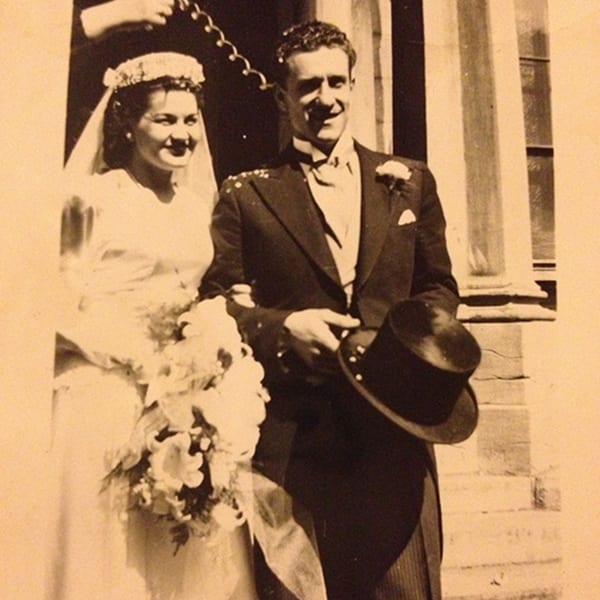 Vintage sepia photo of a smiling bride and groom, confetti falling, outside a building.