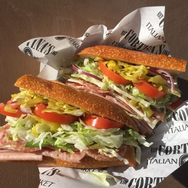 Two Italian subs from Cortina's, filled with meats, cheese, lettuce, tomatoes, onions, and peppers.