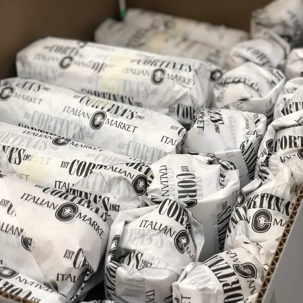 Cortina's Italian Market sandwiches, individually wrapped in branded paper, fill a cardboard box.