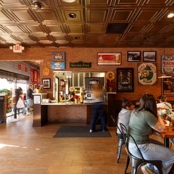 Cortina's Italian Market & Pizzeria interior with brick walls, people dining, and a service counter.