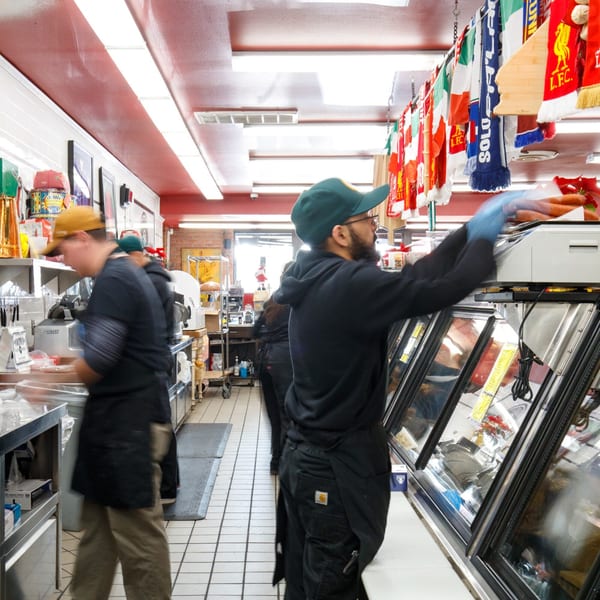 Workers in a bustling Italian market, preparing food behind counters with Italian flags hanging overhead.