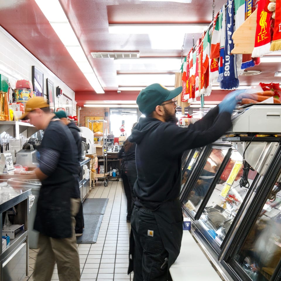 Workers in a bustling Italian market, preparing food behind counters with Italian flags hanging overhead.